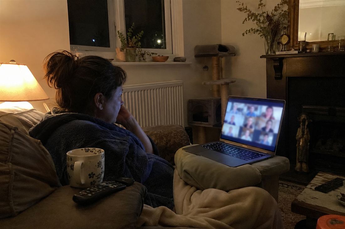 A woman on her sofa at night on a video call with a grid of other women