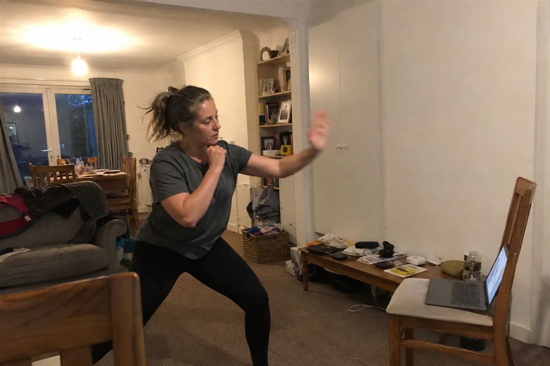 A woman practising palm strikes in her living room, following a lesson on a laptop