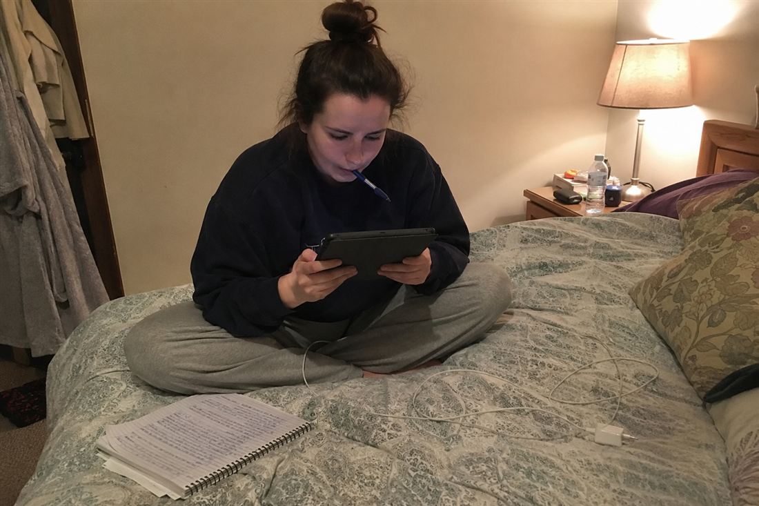 A woman researching on a tablet with a notebook beside her