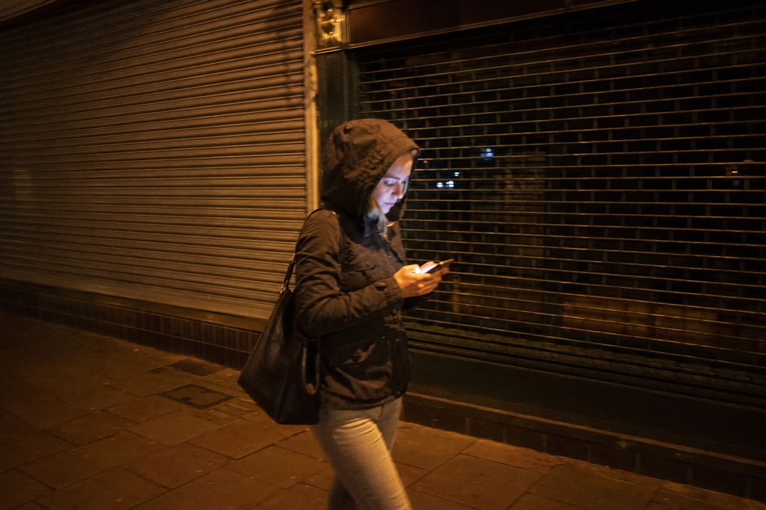 A woman walking past shuttered shops at night, phone in hand